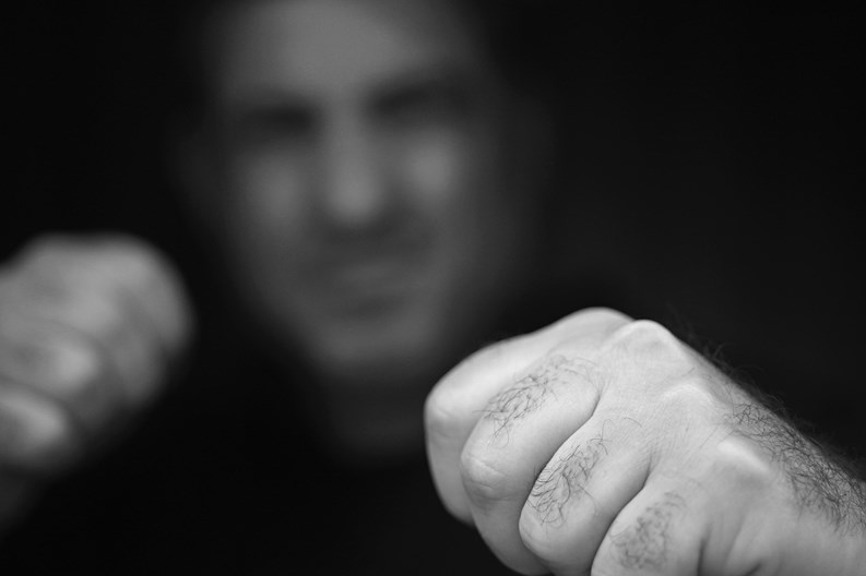 Portrait of abusive aggressive man punching fists from the darkness.