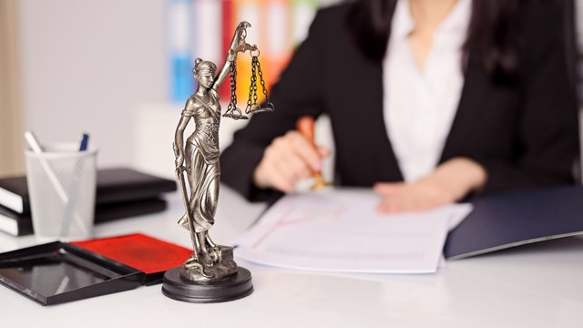 Statuette of Themis - the goddess of justice on lawyer's desk. Lawyer is stamping the document. Law office concept.